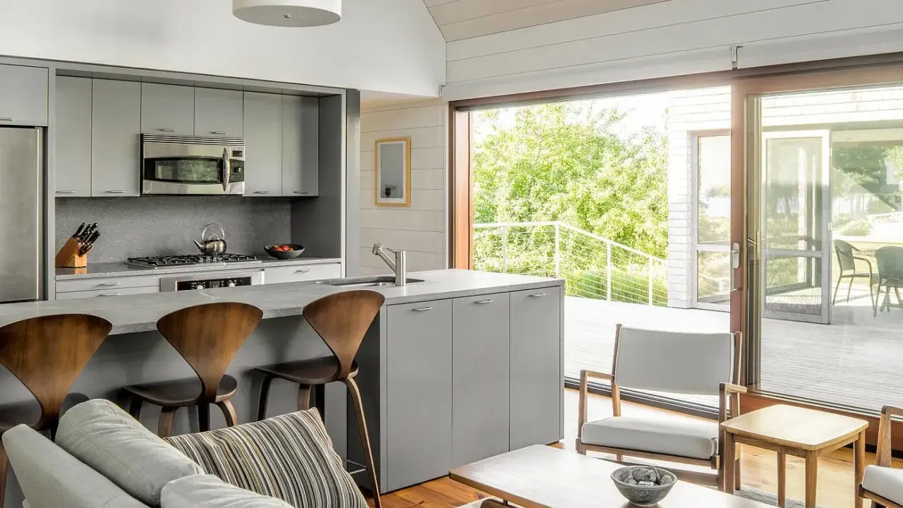 Cocinas abiertas al salón pequeñas con isla gris, taburetes de madera y vistas a un balcón verde.