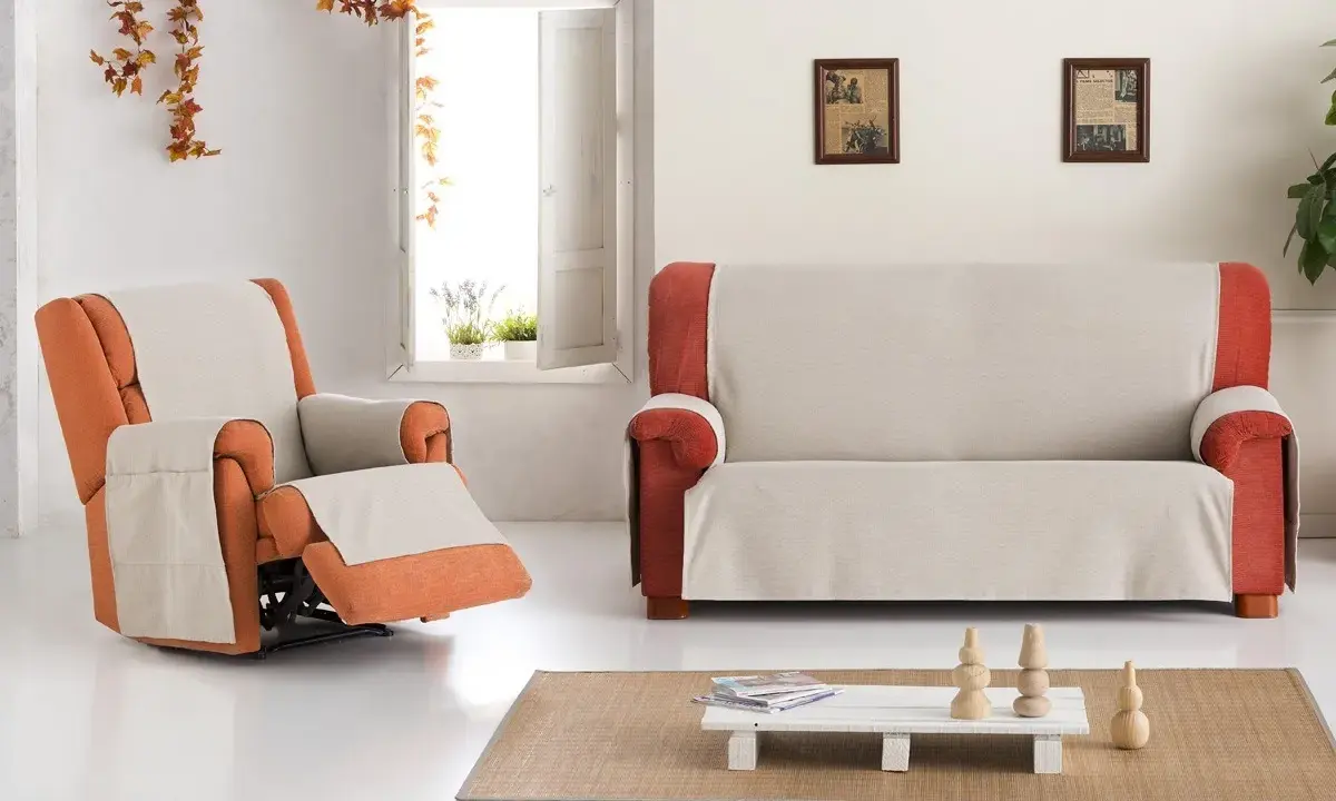 Fundas de sofá Eysa en tonos neutros y naranjas, cubriendo un sillón reclinable y un sofá de dos plazas en un salón luminoso.