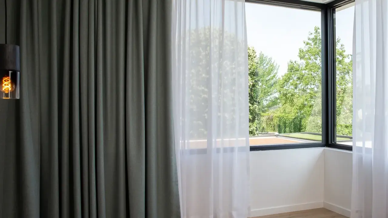 Cortinas bandalux grises y blancas en un dormitorio moderno, con vistas a un jardín frondoso.