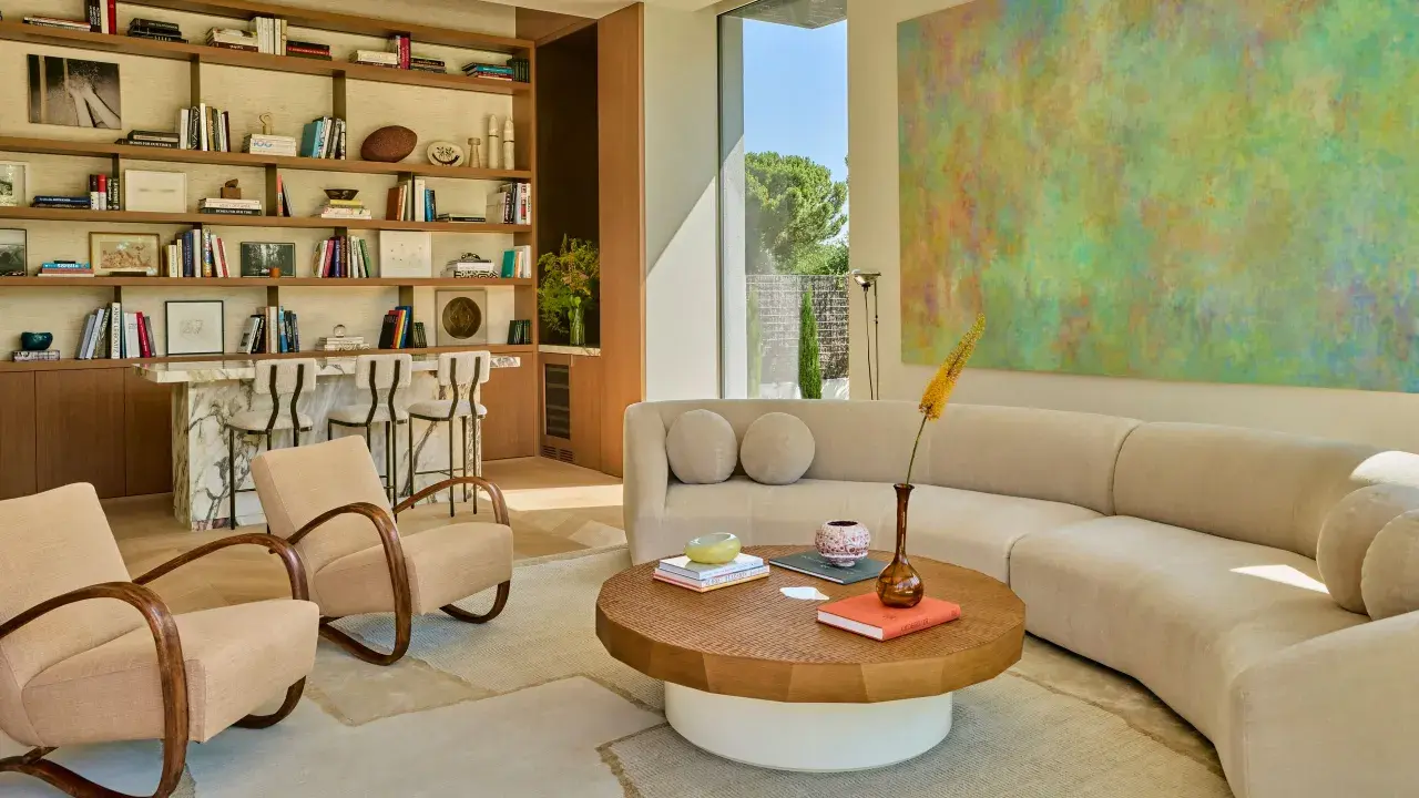 Sofá curvo y sillones de diseño contemporáneo, estanterías llenas de libros y arte abstracto en un salón luminoso.