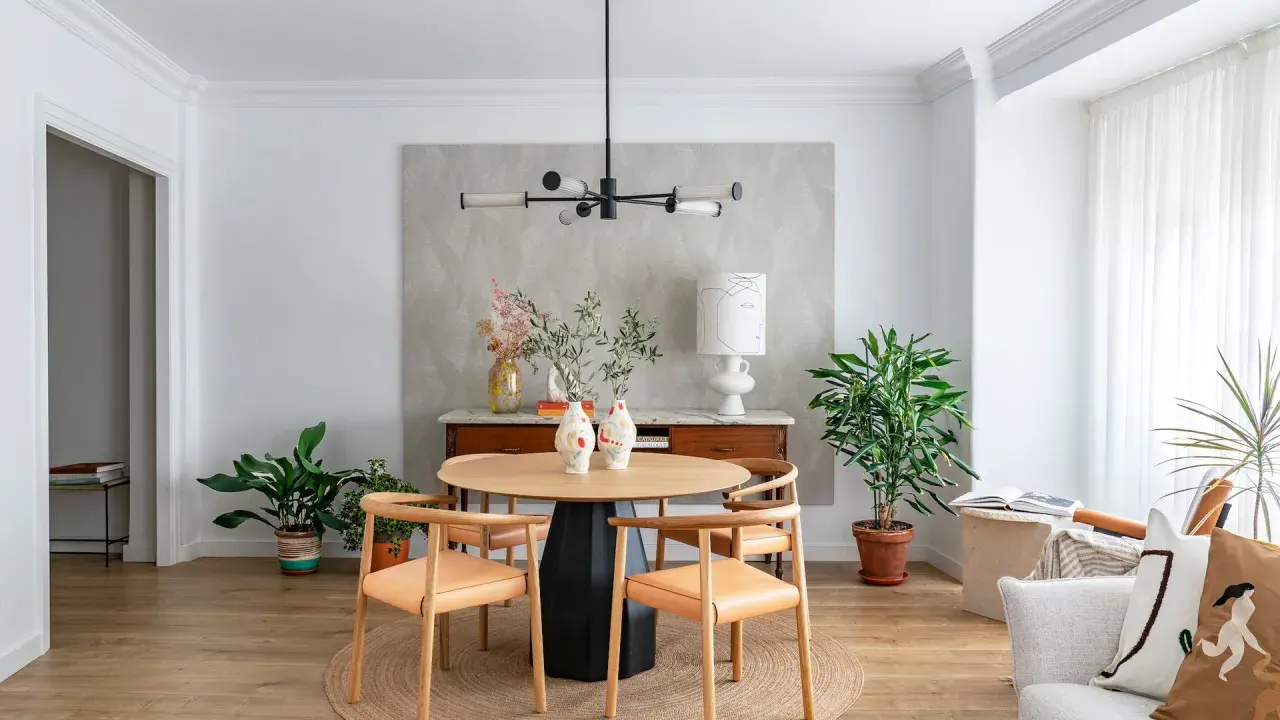 Comedor con mesa redonda de madera, sillas de cuero, lámpara moderna y plantas. Ideal para decorar piso moderno y elegante.