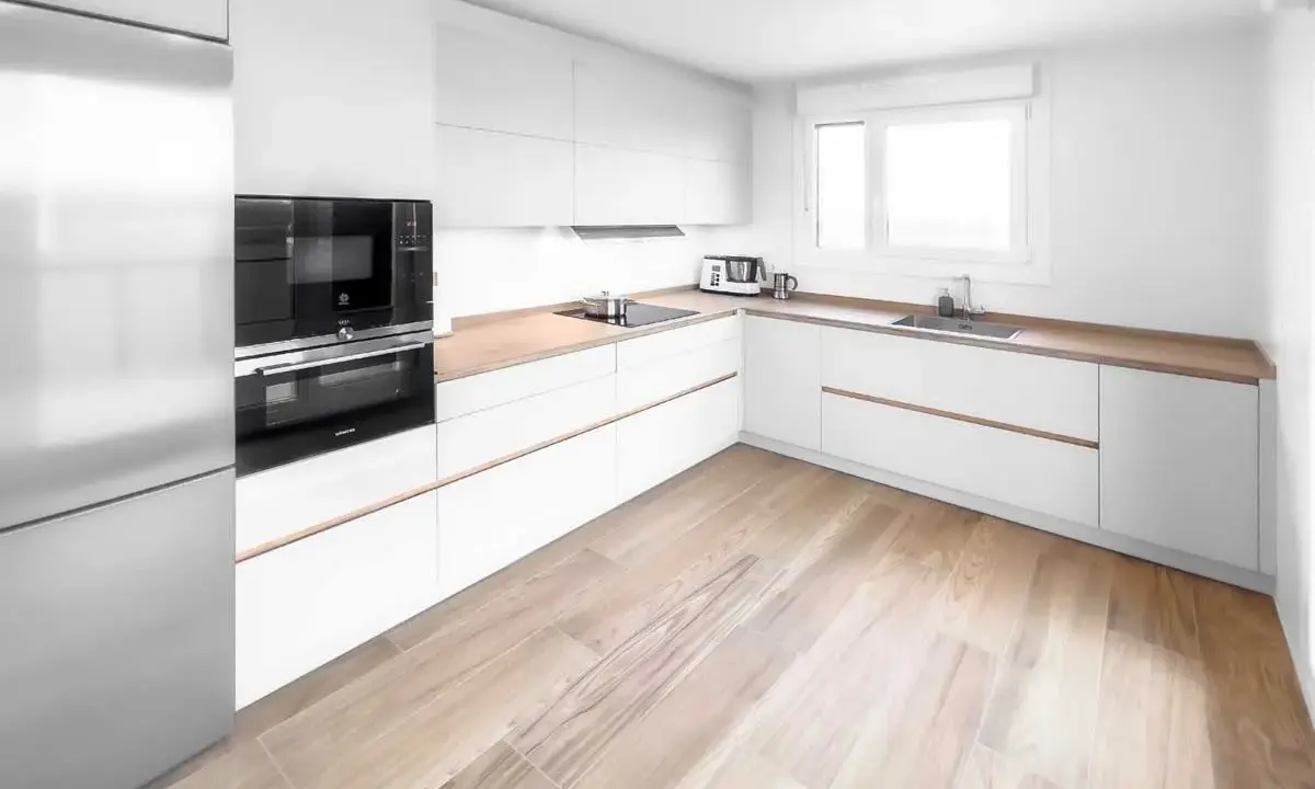 Cocina moderna con armarios blancos y encimeras de madera. El suelo de madera clara complementa perfectamente los suelos para cocinas blancas, creando un ambiente luminoso y acogedor.
