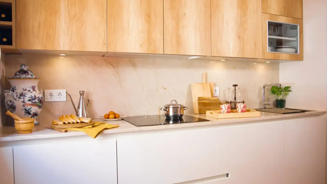 Cocina blanca y madera con encimera de mármol. Hay pan, huevos, una olla y una planta.