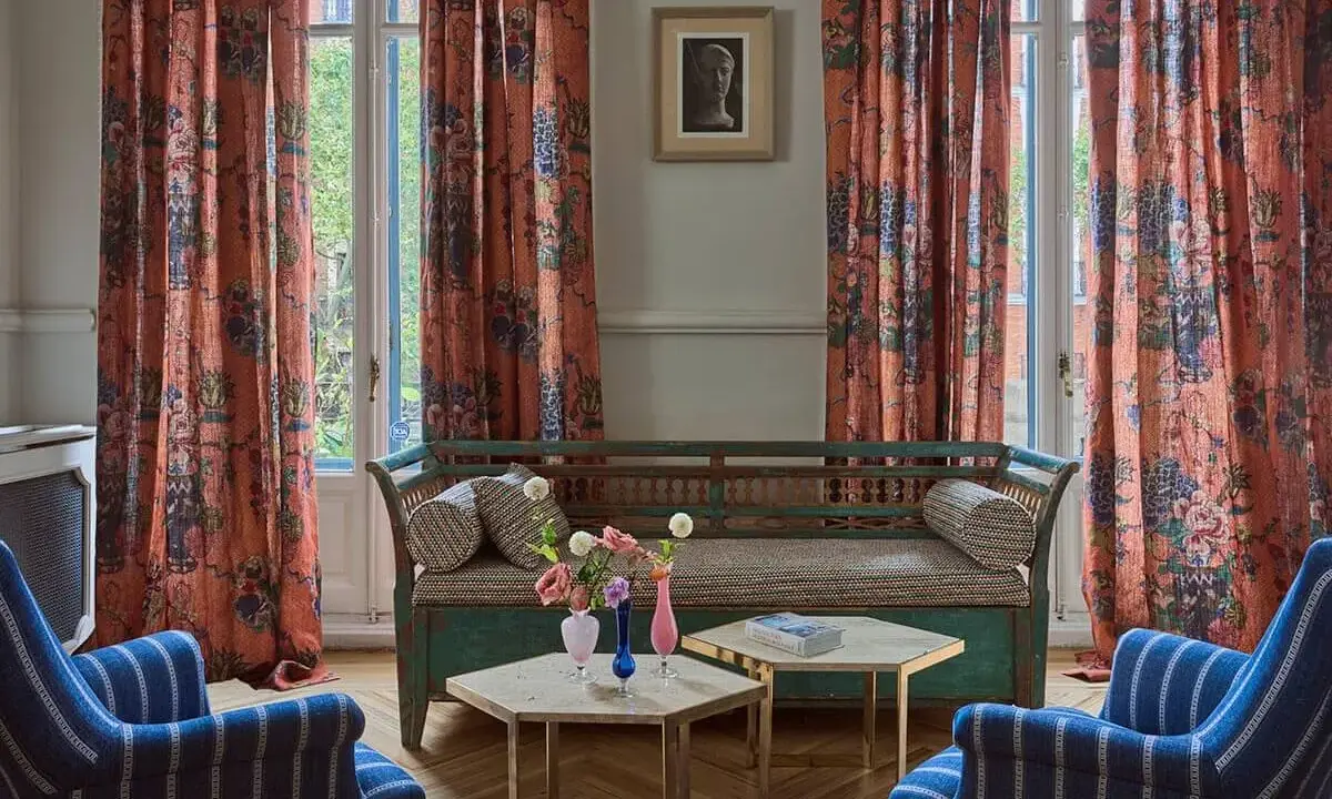 Cortinas de lino estampado con motivos florales y botánicos en tonos anaranjados, complementando un sofá vintage y sillones a rayas.