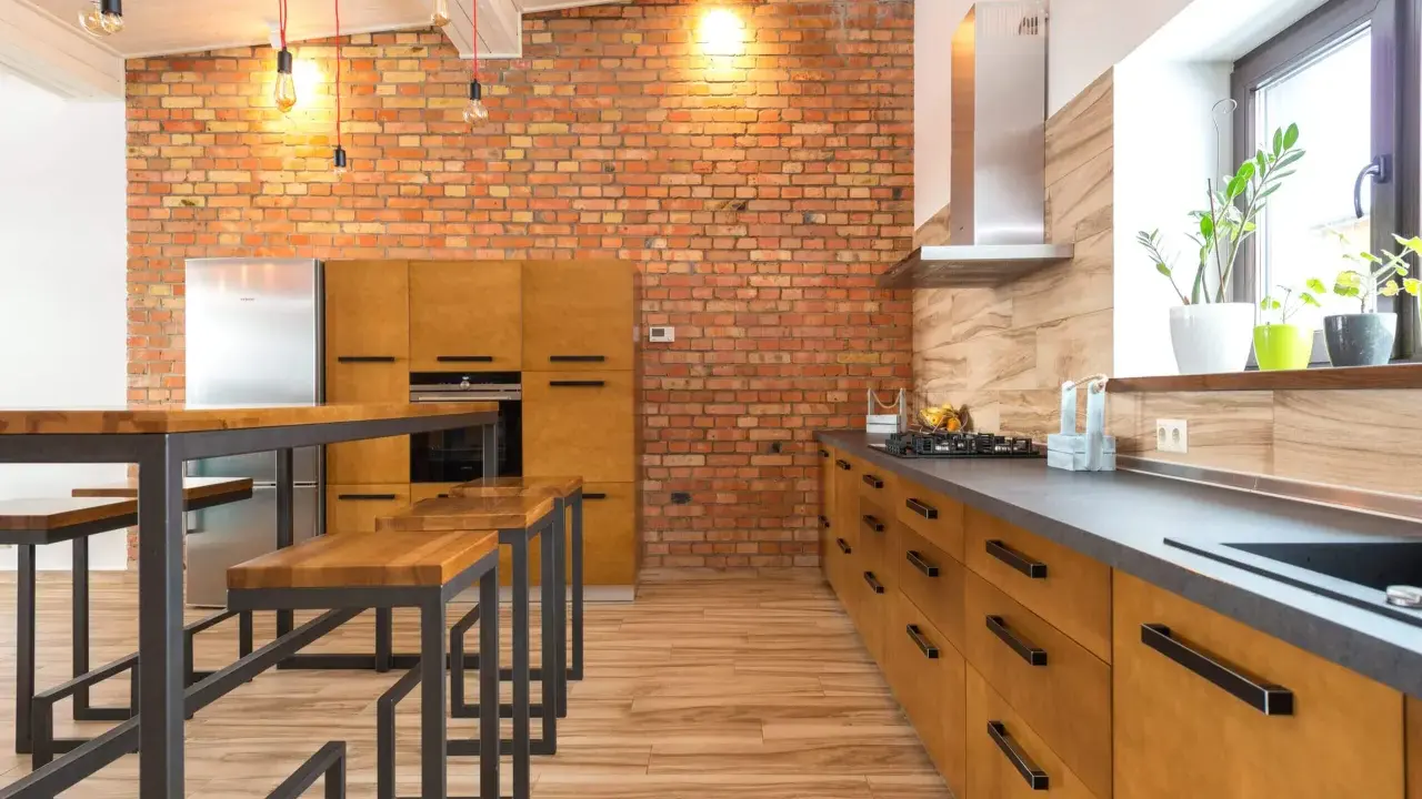 Cocina estilo industrial con paredes de ladrillo visto, muebles de madera y metal, y una isla con bancos.