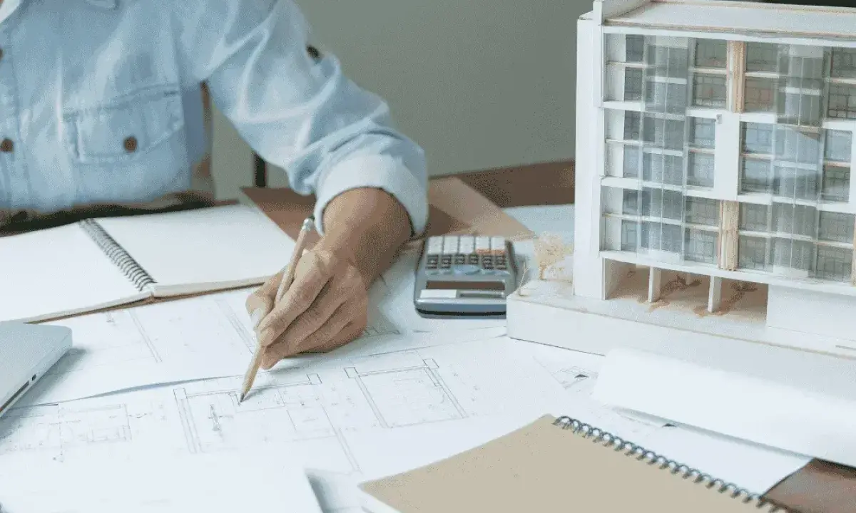 Una arquitecta de interiores dibuja planos junto a una maqueta de edificio.
