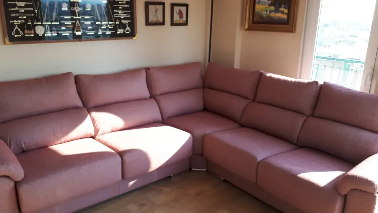 Cómodo sofá rinconera rosa, ideal para decorar salón. En la pared, un cuadro de nudos marineros y pinturas.