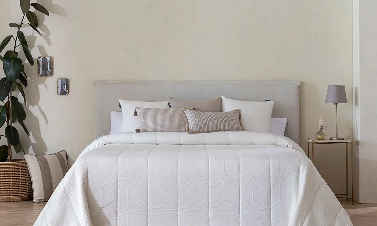 Una cama vestida con una colcha bouti beige de diseño geométrico, cojines y una planta decorativa.