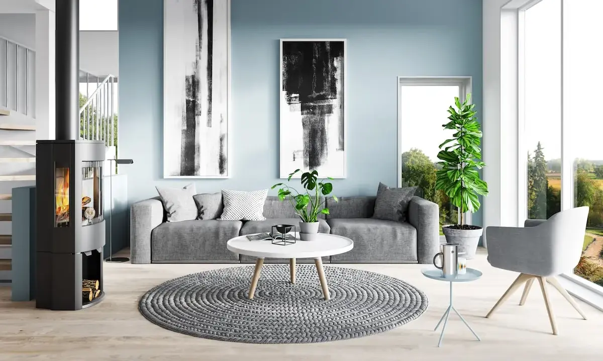 Sala de estar moderna con paredes de color azul polvoriento, sofá gris, chimenea y arte abstracto.