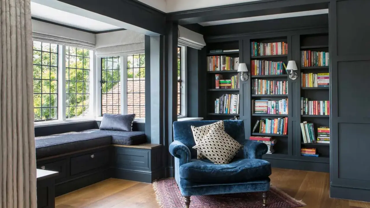 Acogedor rincón lectura salón con sillón azul, ventana con banco y estanterías llenas de libros.