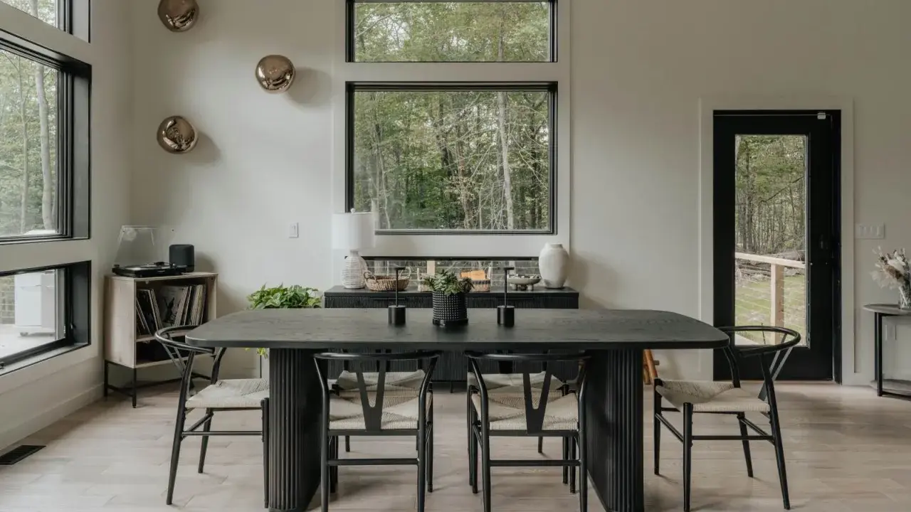 Salón moderno con mesa de comedor negra, sillas de madera y decoración de pared con esferas doradas.