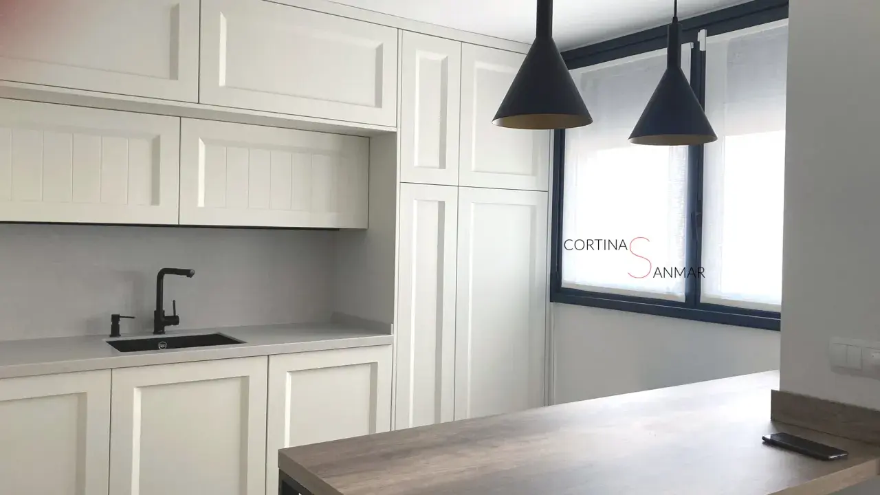 Cocina moderna con armarios blancos, encimera gris, grifo negro y cortinas blancas. Ideas para tu cocina.