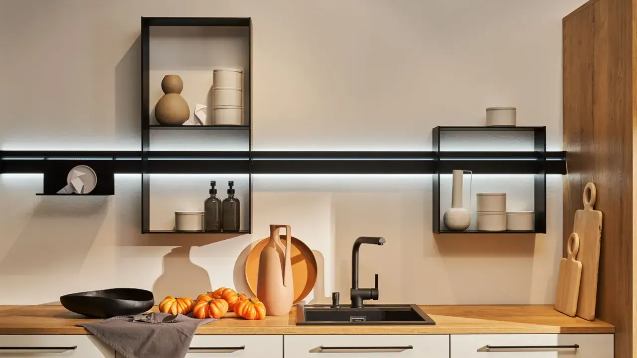 Cocinas sin muebles altos, con estantes flotantes y decoración minimalista. Encimera de madera con fregadero negro, jarrones y calabazas.