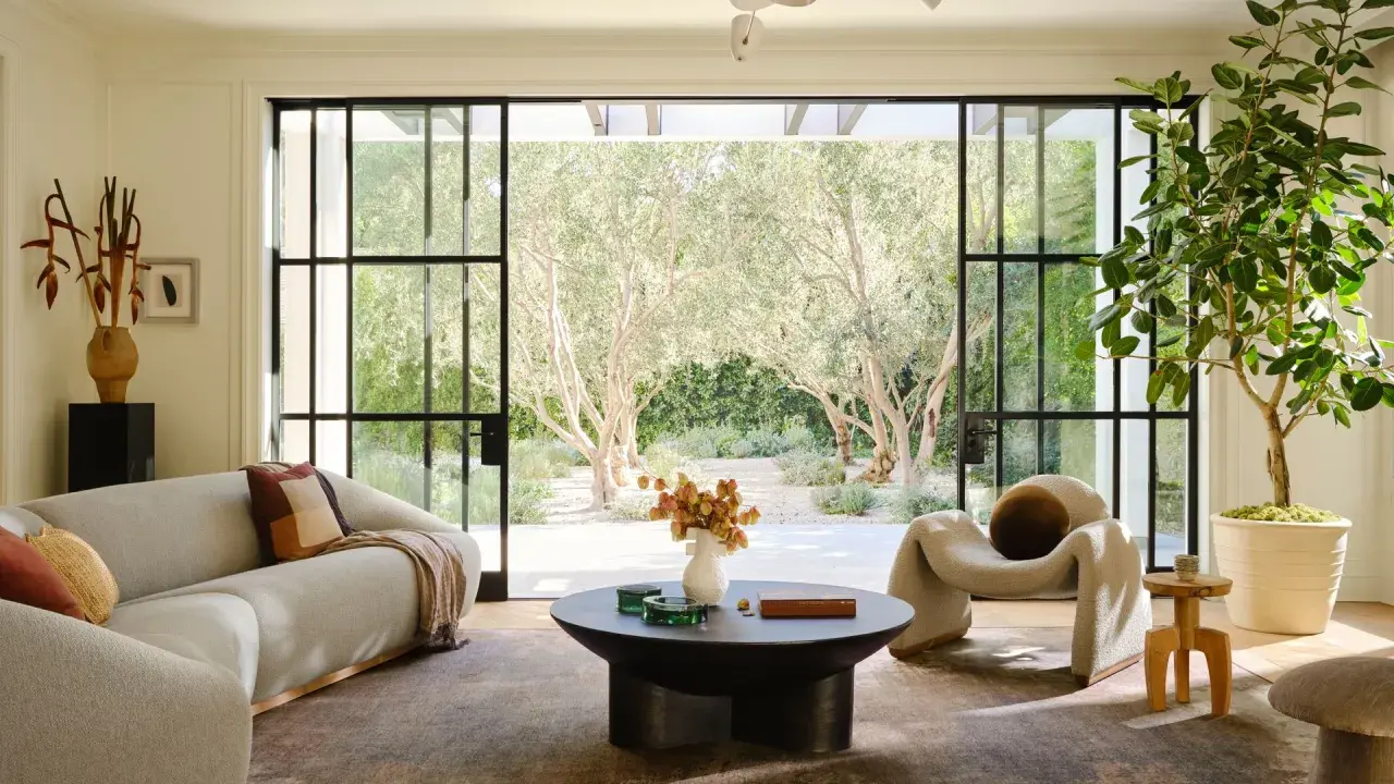 Salones elegantes con sofás curvos, una silla acogedora y grandes ventanales que conectan con un jardín de olivos.