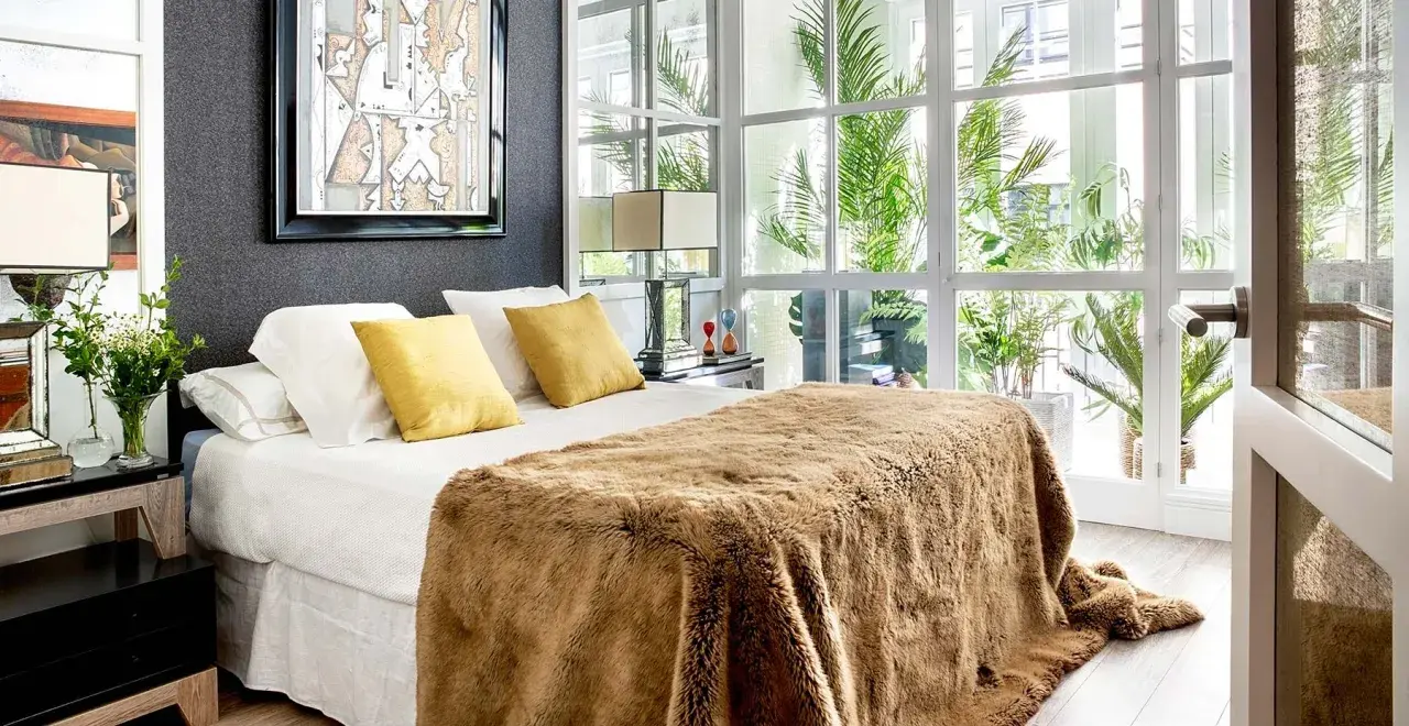 Cama acogedora con manta peluda, cojines amarillos y arte abstracto. Un diseño moderno para decorar habitación con luz natural.