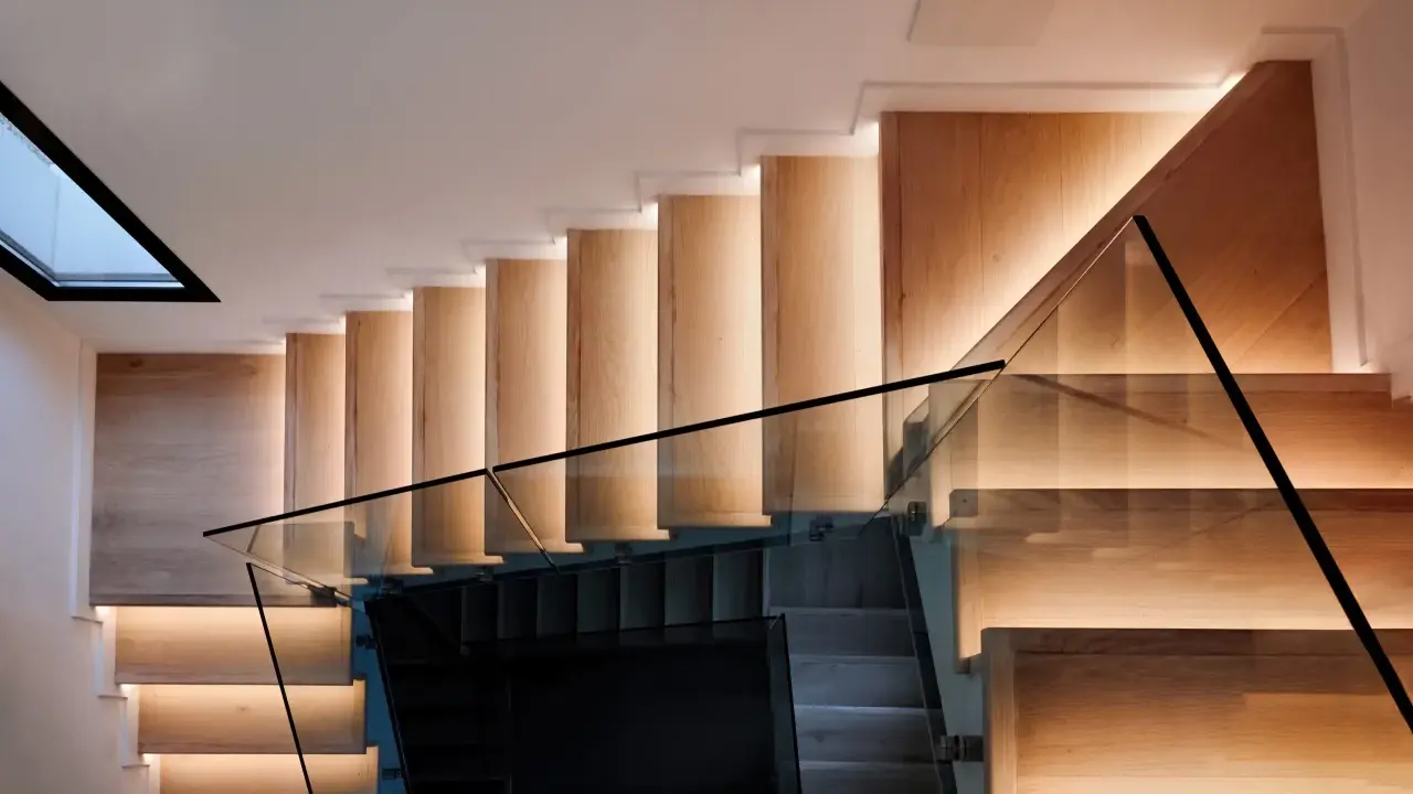 Moderna escalera de madera con iluminación indirecta y barandillas de cristal, vistas en el salón.