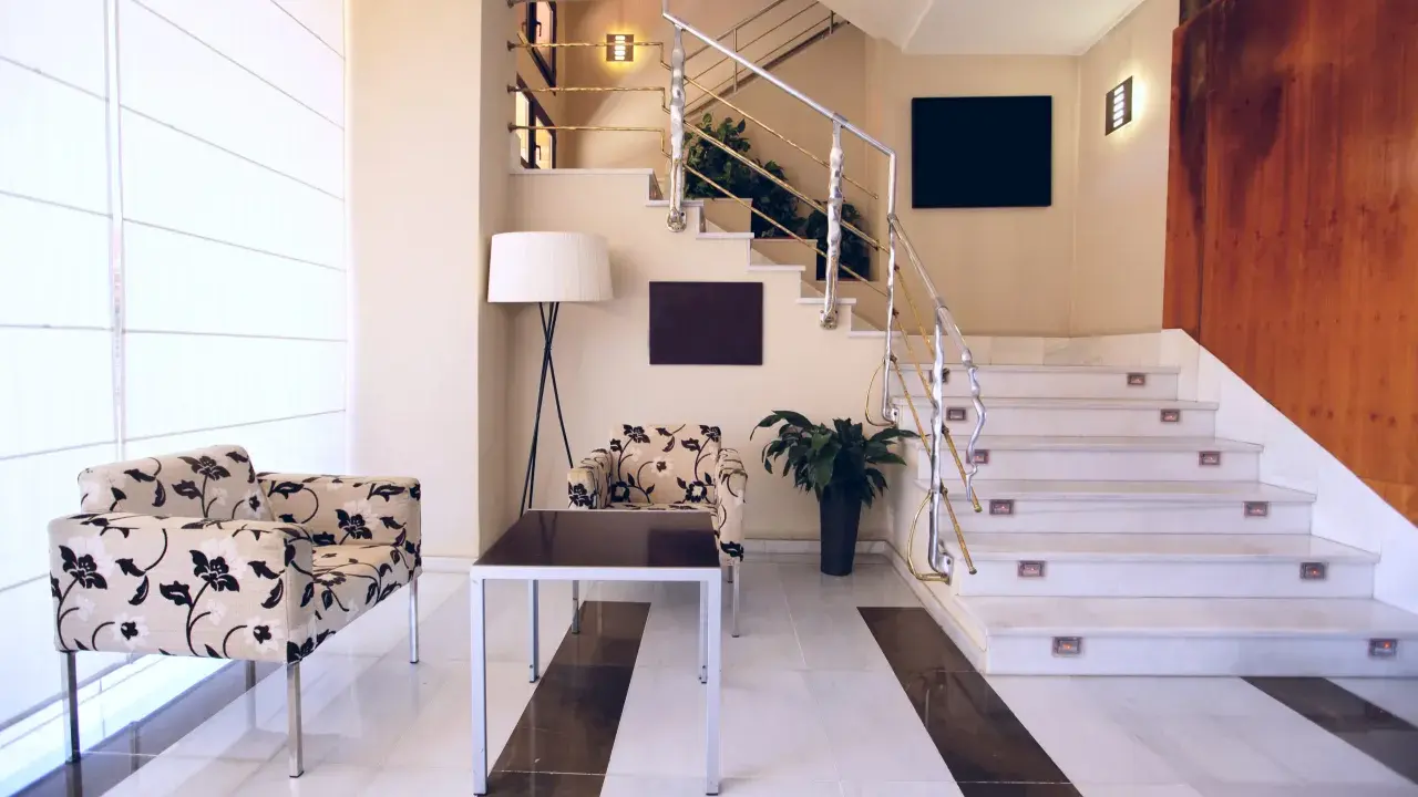 Elegante rellano escalera decoracion con sillones florales y una lámpara de pie. El descansillo escalera cuenta con una barandilla metálica y luces integradas.