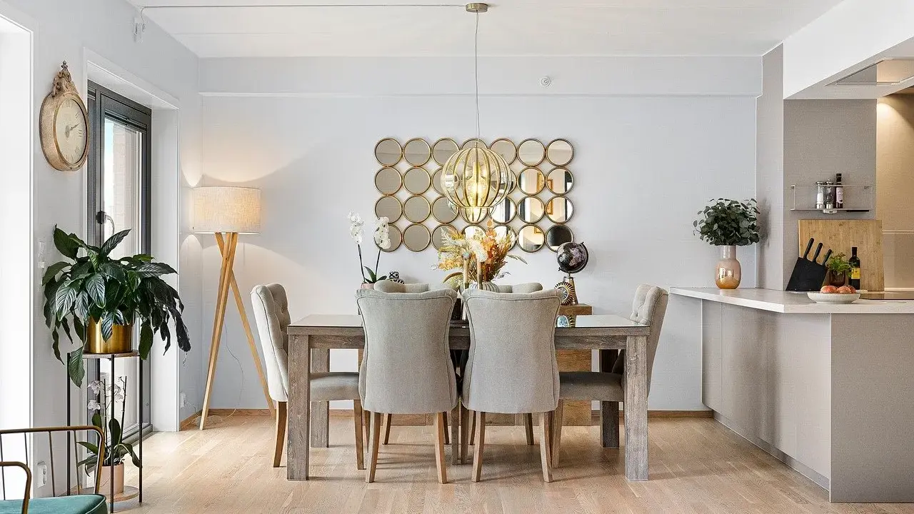 Comedor elegante con mesa de madera y sillas tapizadas, sobre un suelo sisal. Decoración con espejos circulares y lámpara colgante.