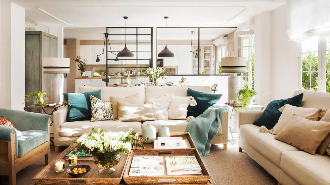 Salones con color: sofás beige, cojines turquesas y mantas suaves crean un ambiente acogedor. Una mesa de centro de madera con flores y libros completa la escena.