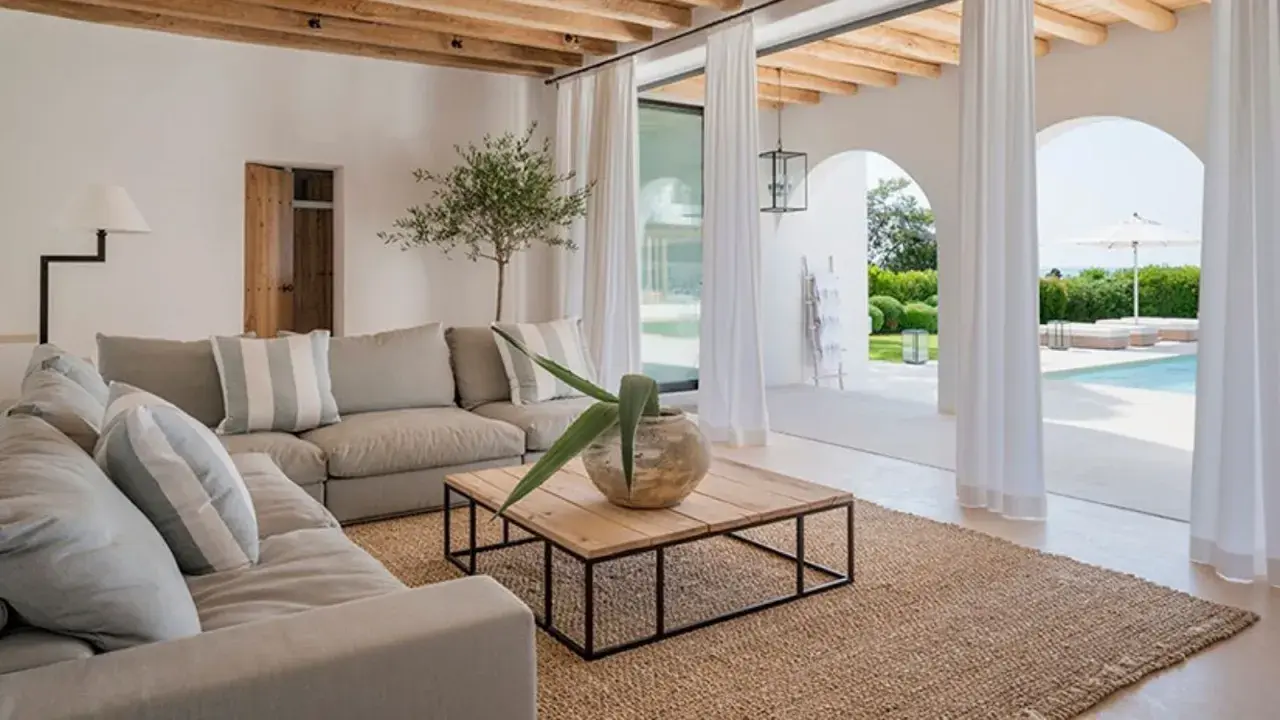 Sofá gris, mesa de centro de madera y alfombra de yute en un salón luminoso con vistas a una piscina.