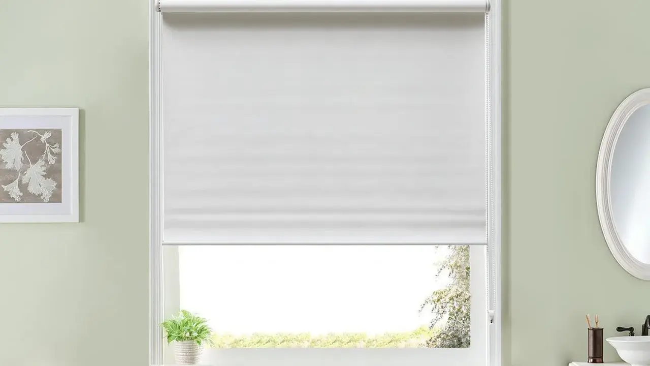 Persiana enrollable blanca que cubre la mayor parte de la ventana. Un pequeño paquete de toallas verdes y blancas descansa en la repisa.