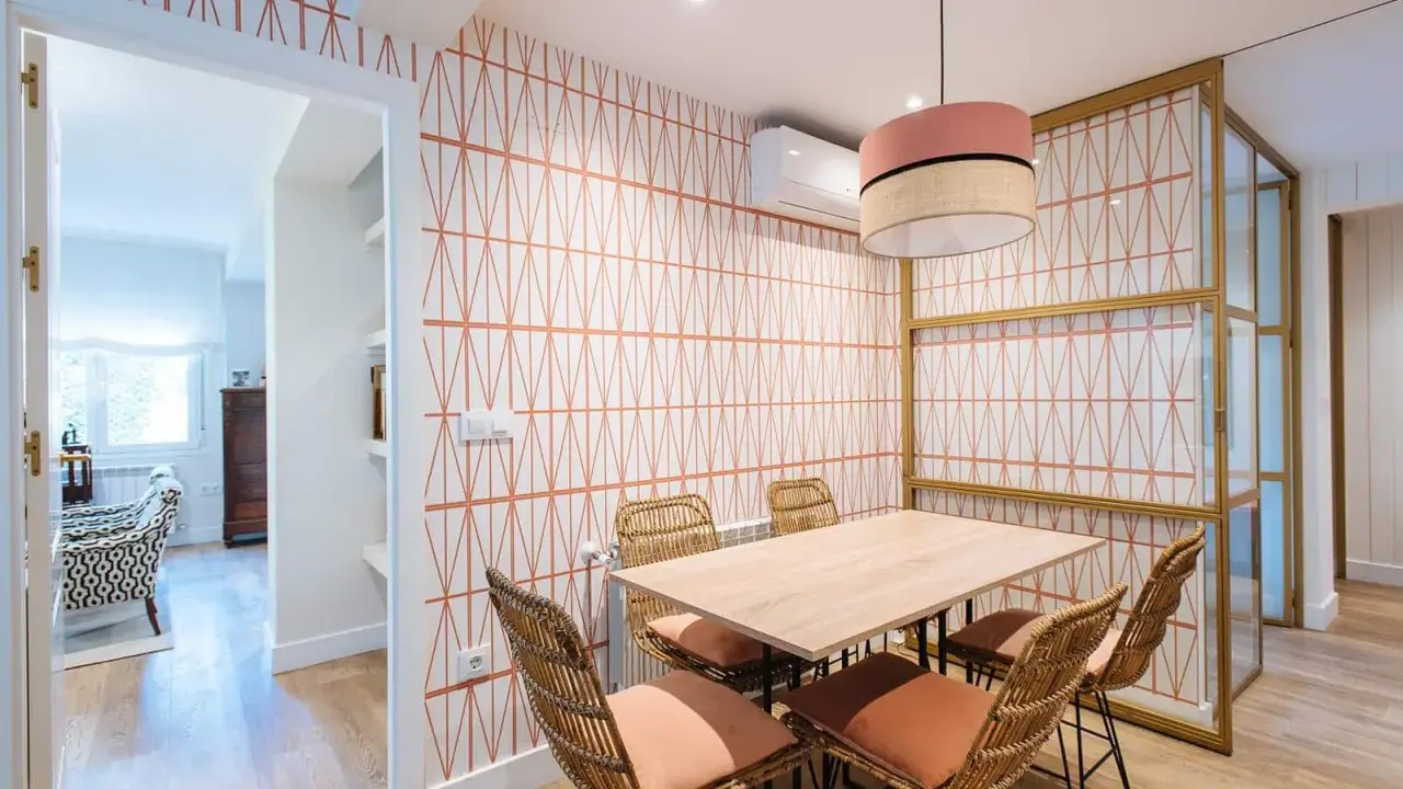 Comedor con papel pintado de rombos naranjas, mesa de madera y sillas de mimbre. Un ejemplo de como poner papel pintado para renovar tu hogar.