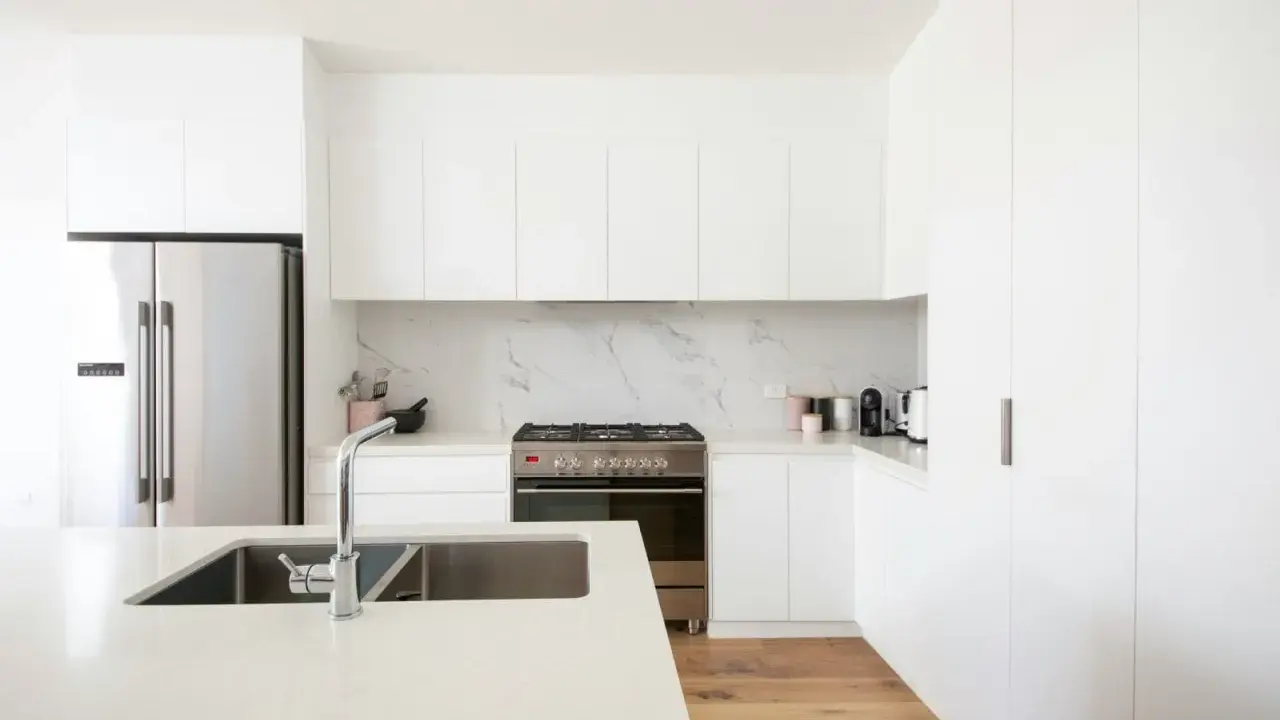 Cocinas blancas elegantes con encimeras de cuarzo, electrodomésticos de acero inoxidable y suelo de madera.