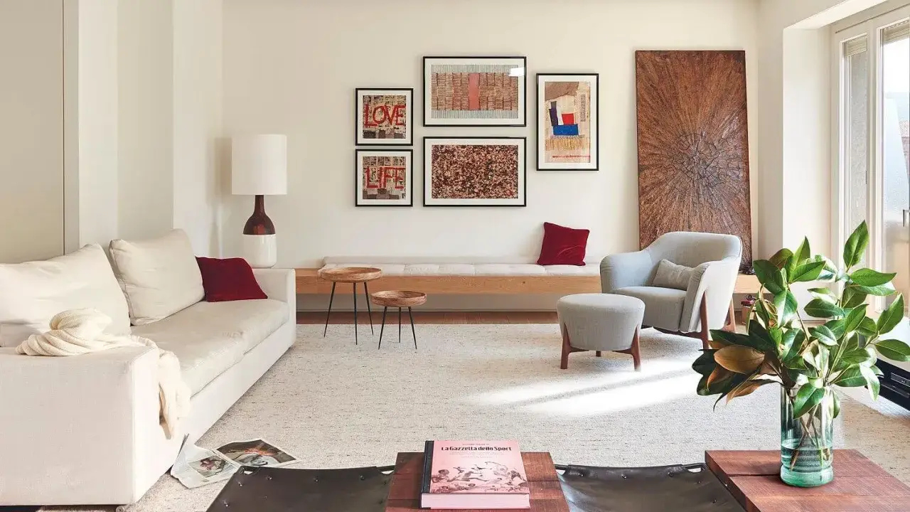 Una composición de cuadros en la pared, con arte abstracto y tipografía, decora este salón moderno junto a un sofá blanco y una butaca gris.