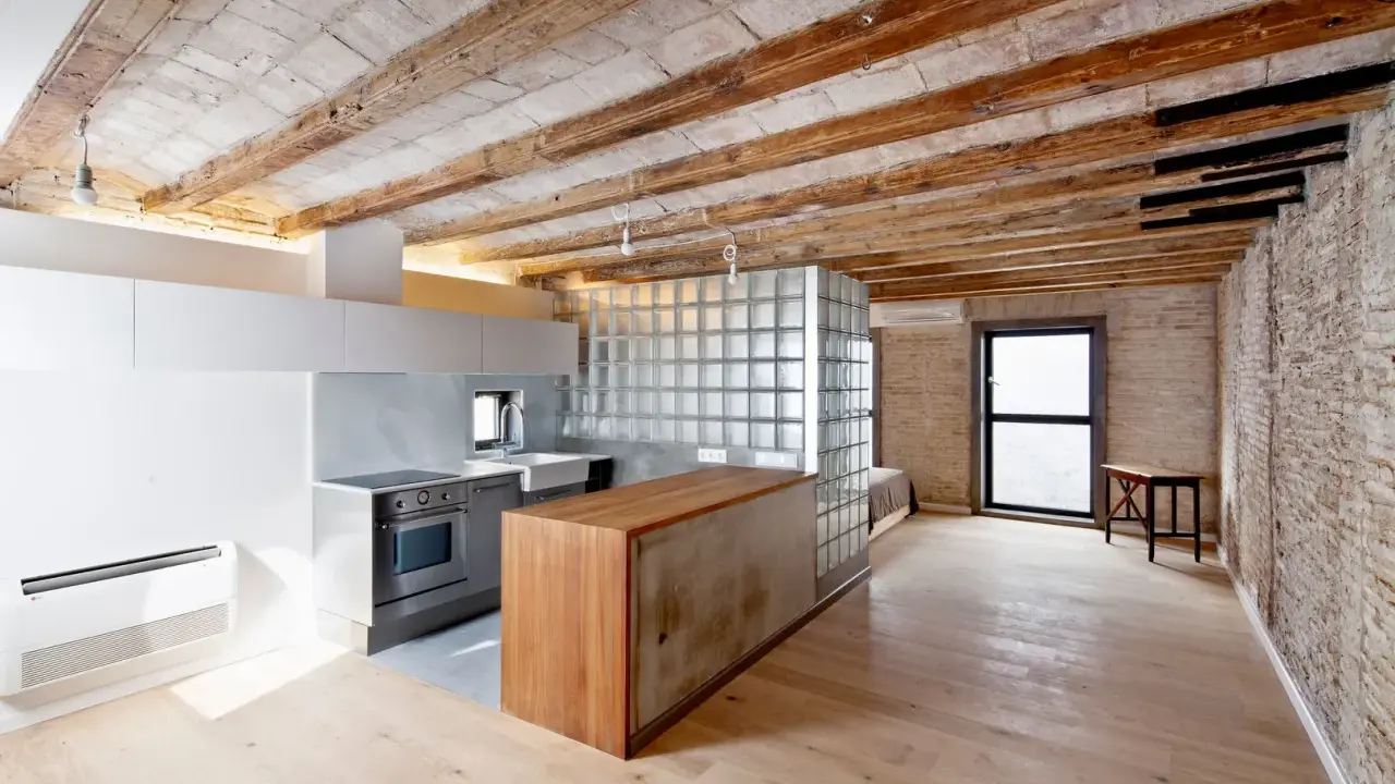 Cocina moderna con isla de madera y cristal, techos de vigas expuestas. Un espacio abierto que evoca la idea de como tirar un tabique para crear amplitud.
