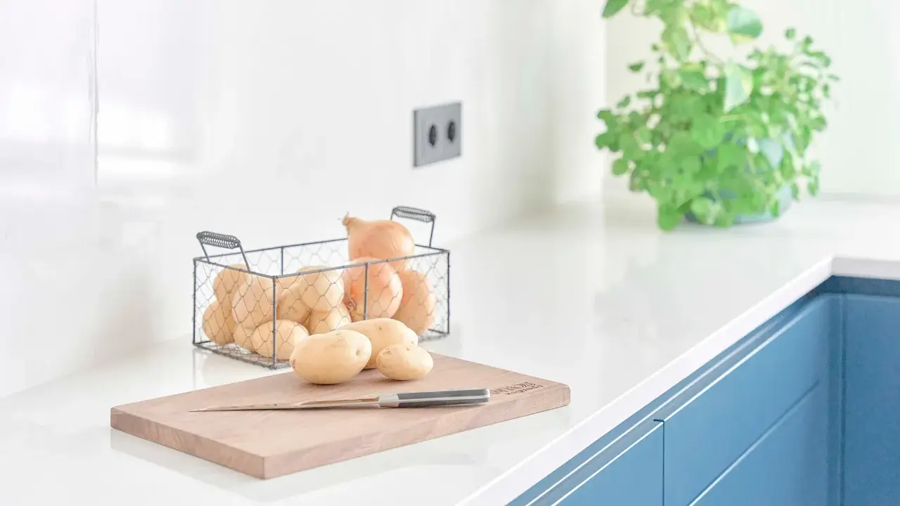 Encimeras de cocina blancas y lisas, con patatas y cebollas listas para cocinar.