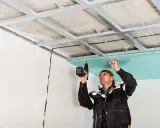 Obrero coloca pladur en techo con taladro.