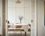 Comedor con mesa cubierta, sillas de madera y una pared en blanco RAL 9010. Un jarrón con ramas decora la mesa.