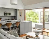 Cocinas abiertas al salón pequeñas con isla gris, taburetes de madera y vistas a un balcón verde.