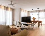 Acogedor salón de 20 metros cuadrados con sofá, mesa de centro, TV, y comedor. Cortinas blancas y suelo de madera crean un ambiente luminoso.