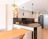 Moderna cocina en L con isla, electrodomésticos integrados, encimera de cuarzo y mesa de madera.