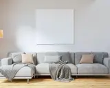 Un sofá gris moderno, listo para decorar con cojines y mantas, junto a una lámpara y una planta.