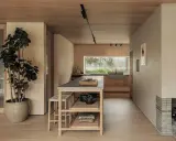 Un acogedor salón cocina pequeño con isla central, mucha madera y una gran ventana al exterior.