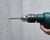 Taladrando hormigón con un taladro. La broca se adentra en la pared texturizada.