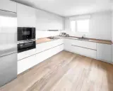 Cocina moderna con armarios blancos y encimeras de madera. El suelo de madera clara complementa perfectamente los suelos para cocinas blancas, creando un ambiente luminoso y acogedor.