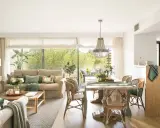 Elegante decoracion salon con sofás, mesa de comedor de madera, sillas de mimbre y gran ventanal con vistas al exterior.
