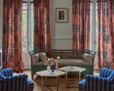 Cortinas de lino estampado con motivos florales y botánicos en tonos anaranjados, complementando un sofá vintage y sillones a rayas.