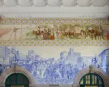 Azulejos de Oporto narran la historia: un tren antiguo, gente vestida de época y una procesión militar en azul y blanco.
