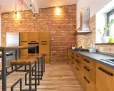 Cocina estilo industrial con paredes de ladrillo visto, muebles de madera y metal, y una isla con bancos.