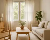Sofá beige y silla de madera con asiento de lino tejido, junto a una mesa de centro de madera y cortinas claras.