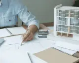Una arquitecta de interiores dibuja planos junto a una maqueta de edificio.