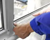 Manos ajustando el burlete para aislar ventanas, mejorando la eficiencia energética del hogar.