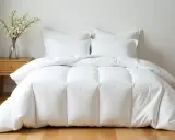 Cama impecable con edredón plumón oca blanco y cojines. Un jarrón con flores decora la mesita de noche.