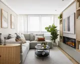 Acogedora decoracion salon pequeño con sofá gris, chimenea moderna y estanterías de madera.