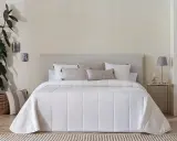 Una cama vestida con una colcha bouti beige de diseño geométrico, cojines y una planta decorativa.