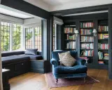 Acogedor rincón lectura salón con sillón azul, ventana con banco y estanterías llenas de libros.